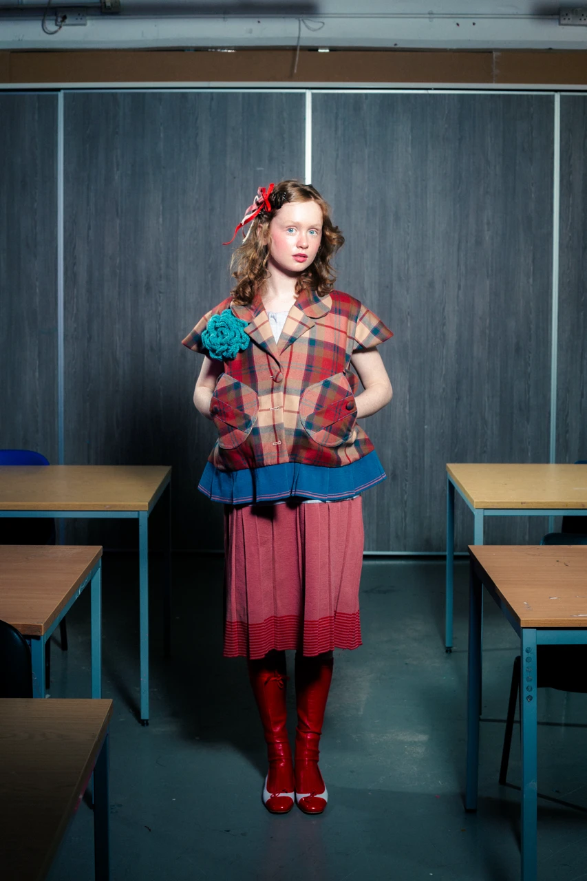 Isolt in *Look 3*, wool Peblum school coat with knitted pleats, cotton school dress with knitted pleats.