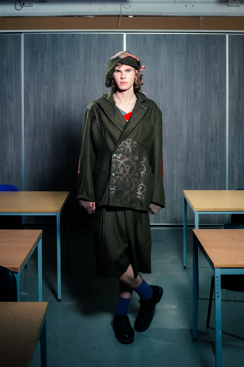 Arjius in *Look 2*, wool double breasted blazer with leather and Merino appliqué, pleated fold-over school shorts with leather appliqué. Styled with over-sized Baker Boy hat.