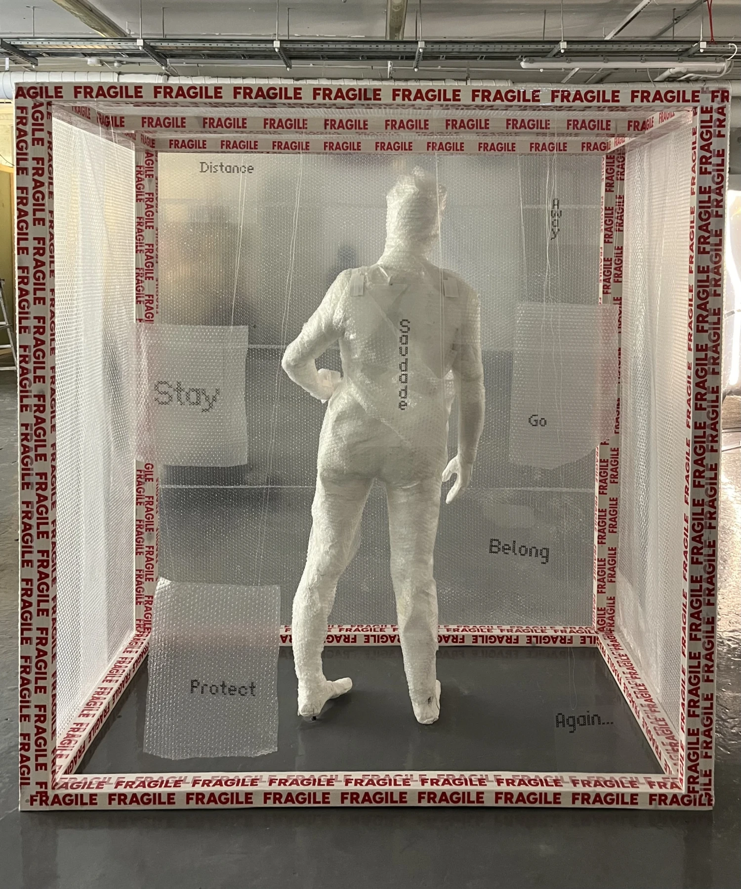 Front view of installation showing suspended text and standing body form.