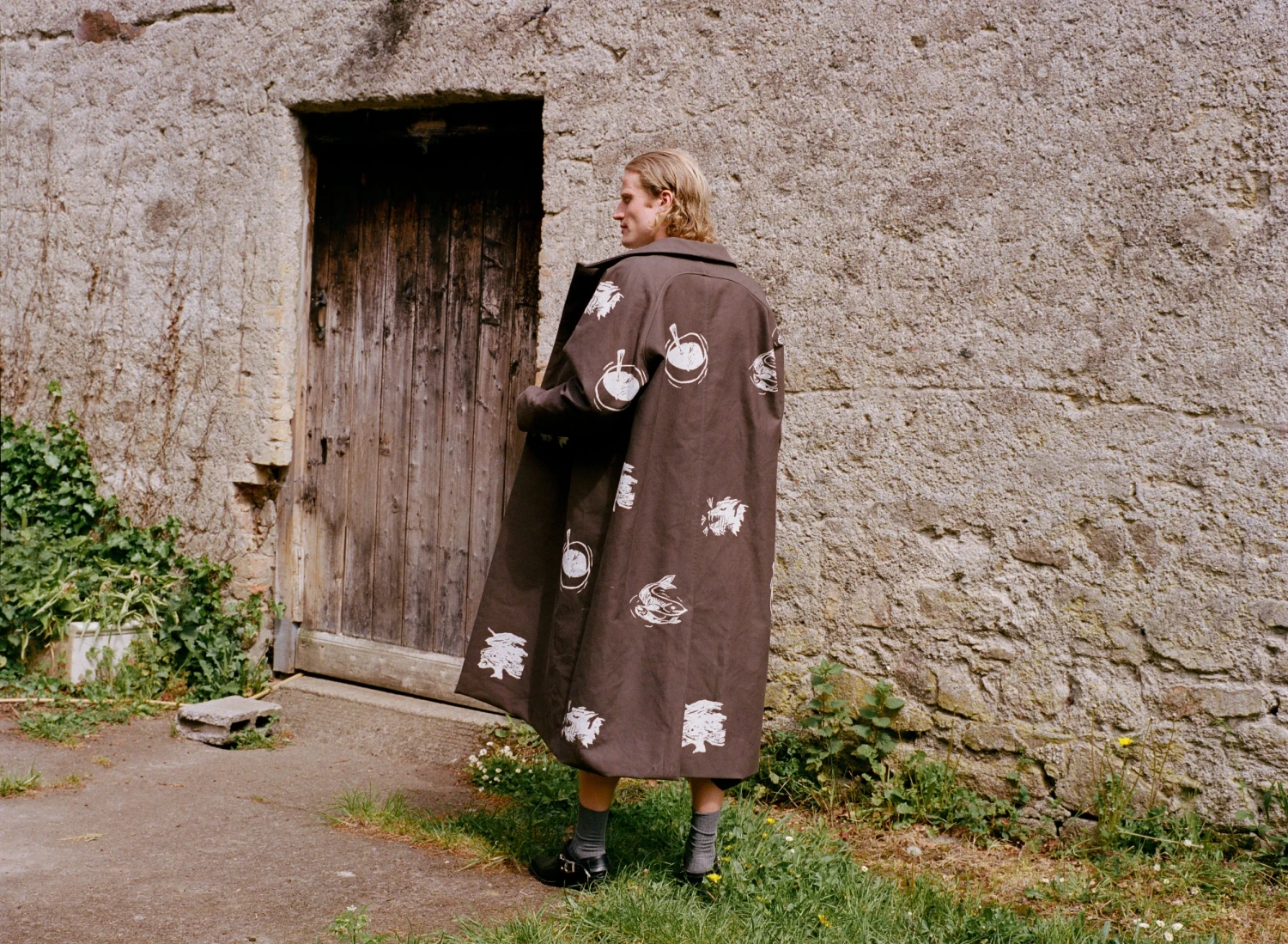 Luke wearing screen printed cotton drill trench coat, embroidered cotton jersey tshirt and embroidered short trousers. Image credit: Ella O'Brien.