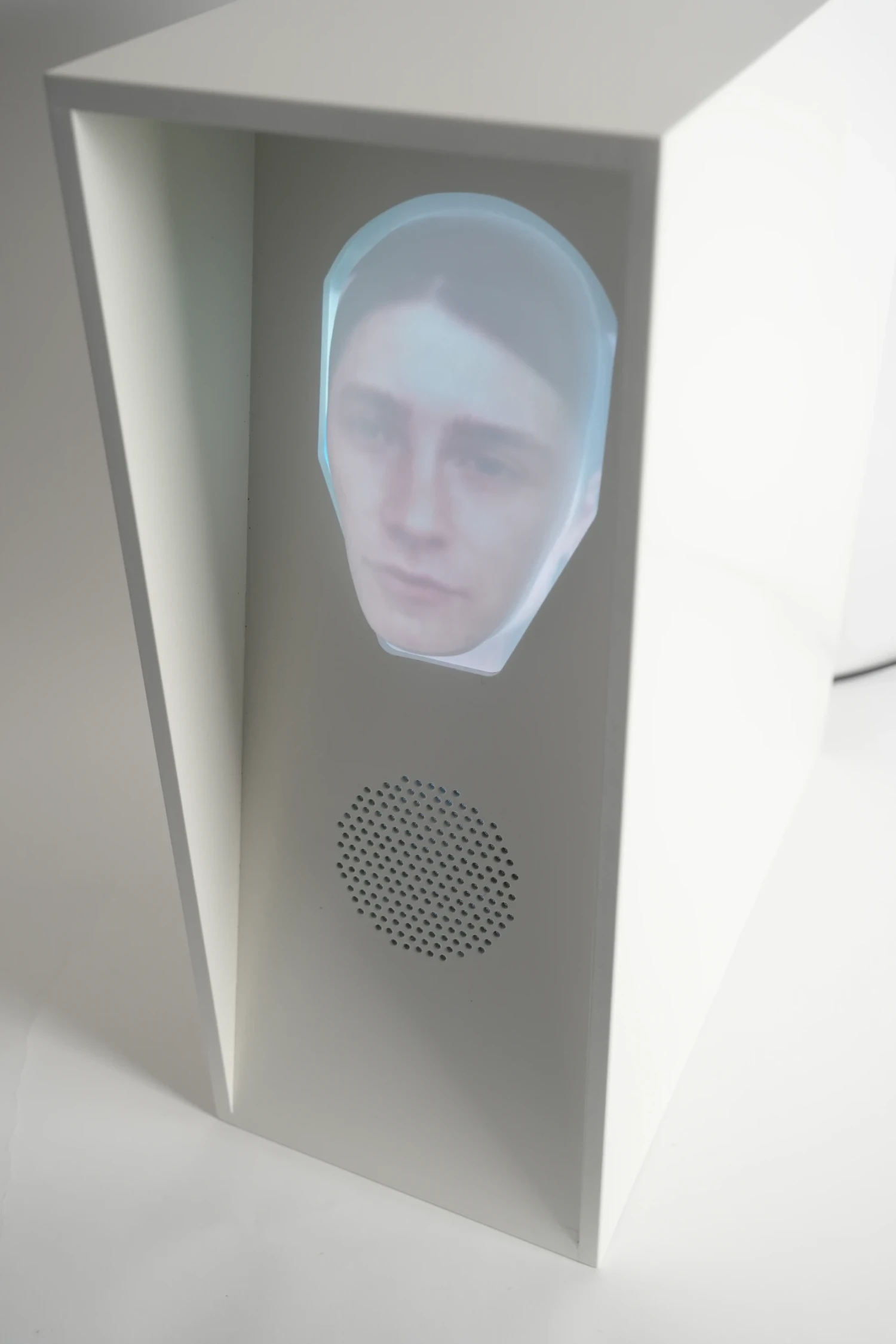 Spray-coated white wood housing with front-facing projected mask and embedded speaker, 50 × 22 × 60 cm.